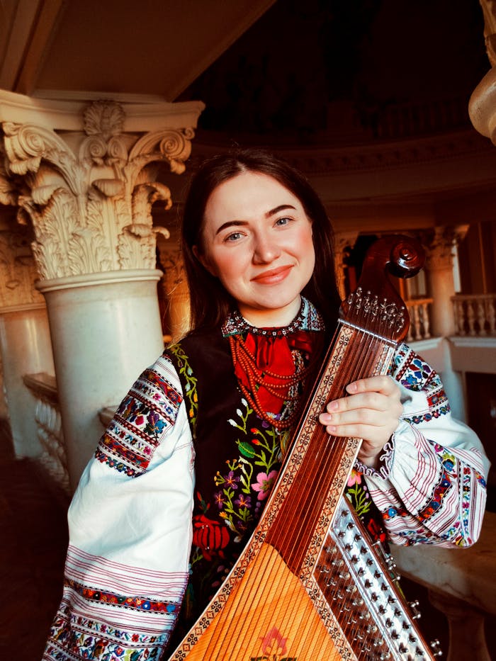 Charming young woman in traditional Polish folk attire, posing with a string instrument indoors.